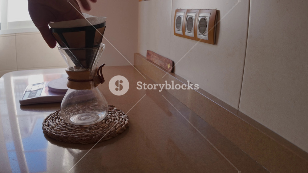 Capturing the serene moments of a daily morning routine, a person meticulously prepares a pour-over coffee using a Chemex brewer. The focus is on the mindful process and the anticipation of a fresh brew.