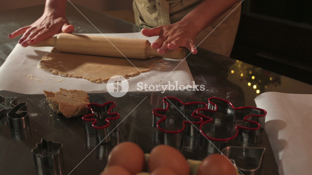 Woman in chef's apron is preparing gingerbread cookies and gingerbread man cookies, surrounded by Christmas lights. The concept of upcoming