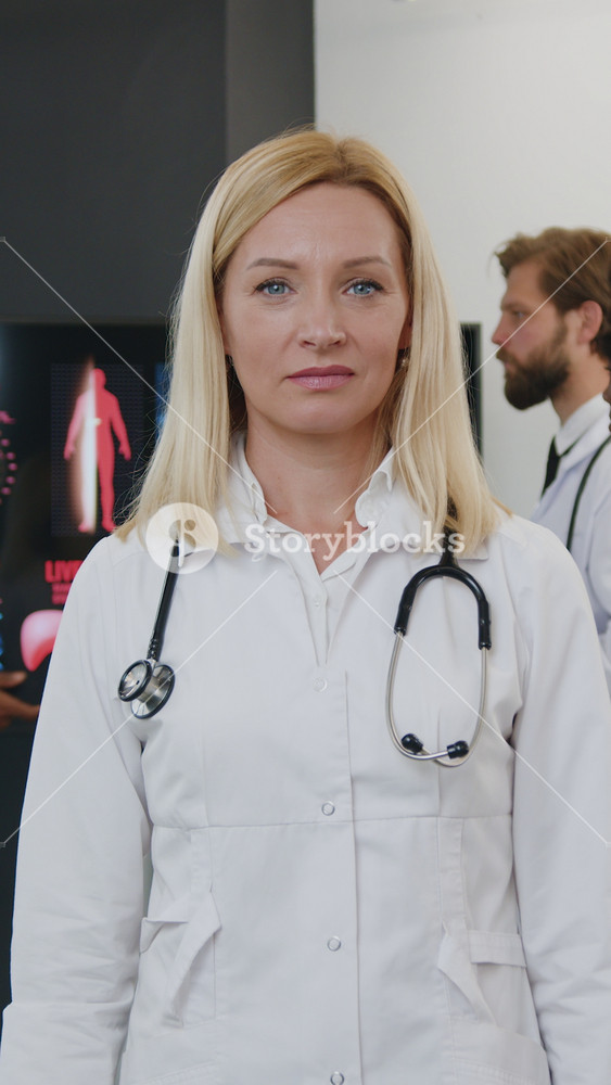 Good-looking purposeful high-skilled adult light-haired female doctor standing in front of camera with crossed arms near her multiracial