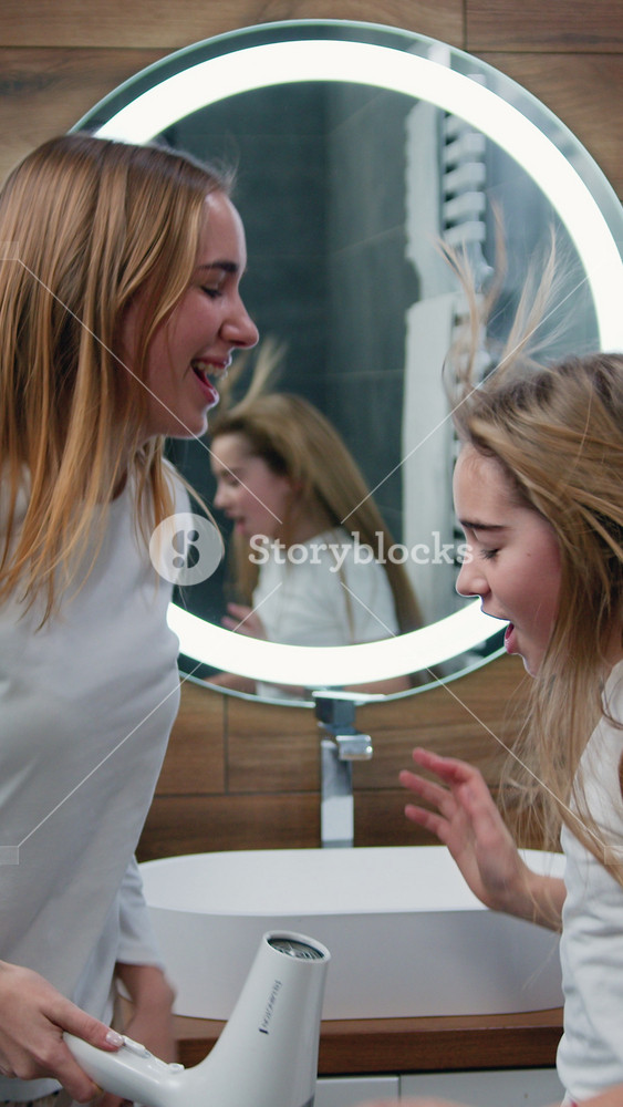 Joyful young woman and little girl in a white robe dries her hair, sings and dances in the bathroom at home. Caucasian girls in playful mood