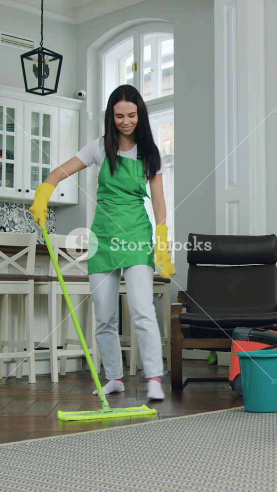 Portrait of adorable happy professional positive female cleaner in green apron which cleaning up client's contemporary apartment and washing
