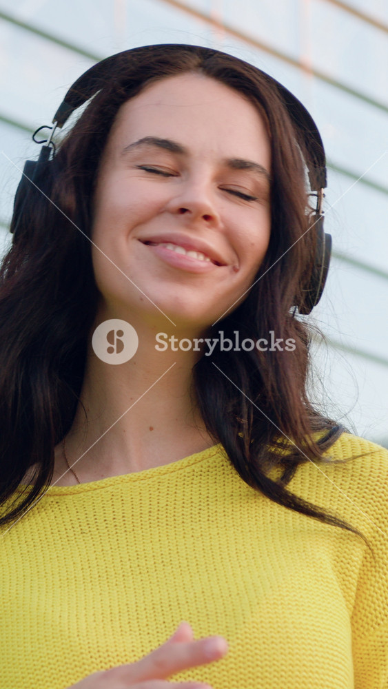 Good-looking carefree satisfied 30-aged modern brunette dressed in trendy knitted sweater listening inflammatory music in earphones on the