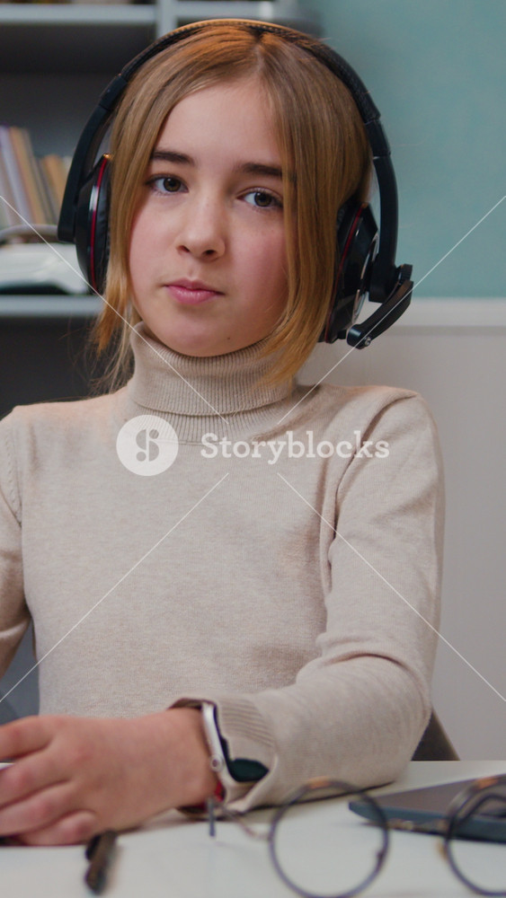 Smart beautiful caucasian 10 years old girl wearing headset watching media on tablet sitting by table in living room at home. Preteeen girl