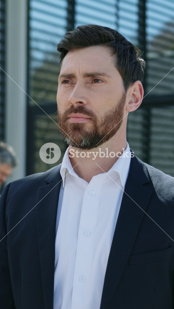Close-up portrait of attractive serious handsome Caucasian man in suit looking directly at camera on background of business people. Work