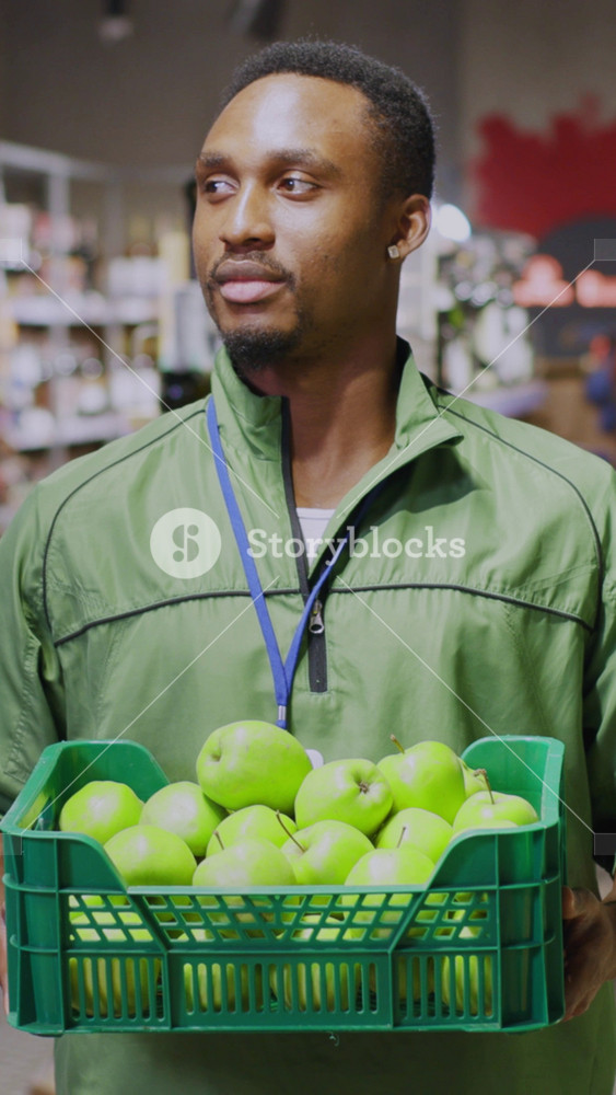 Portrait of happy employee afro-american young worker holding basket full of fresh fruits at organic marketplace supermarket grocery store.