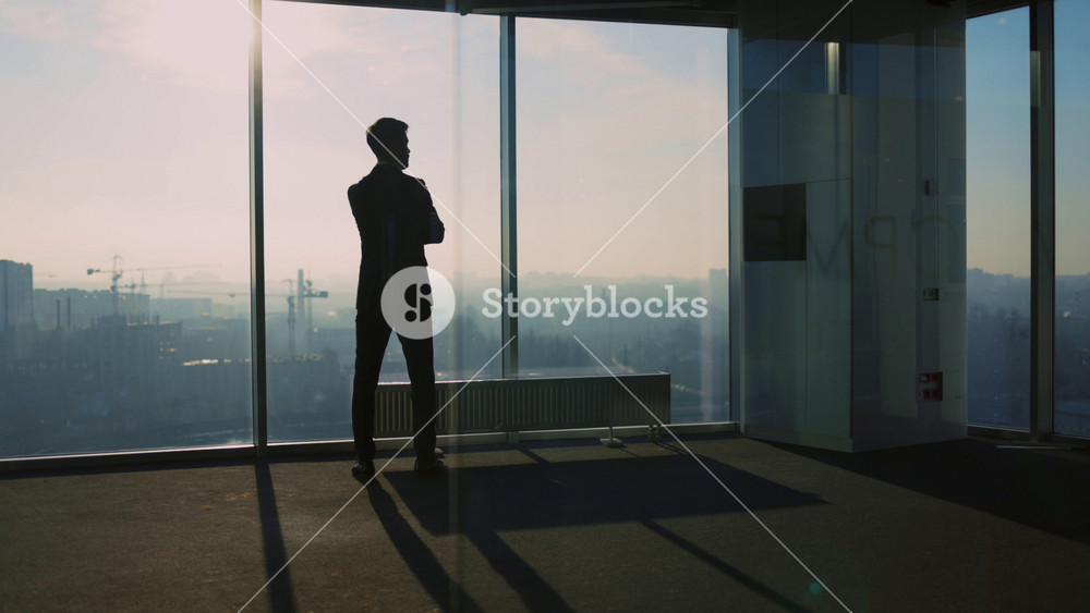 Young pensive businessman looking out of window contemplating future business ideas for construction new city buildings. Office cabinet