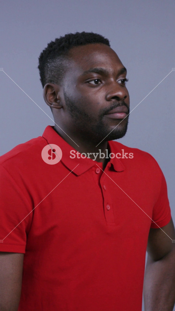Serious thoughtful Afro-American man in bright red shirt stands still, then looks straight to camera on grey background. Male beauty. Male