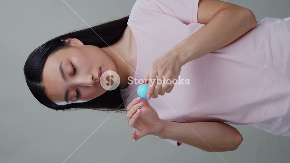 Portrait of attractive korean young woman applying hydrating lip balm with ball smiling and giving air kiss to camera isolated on background