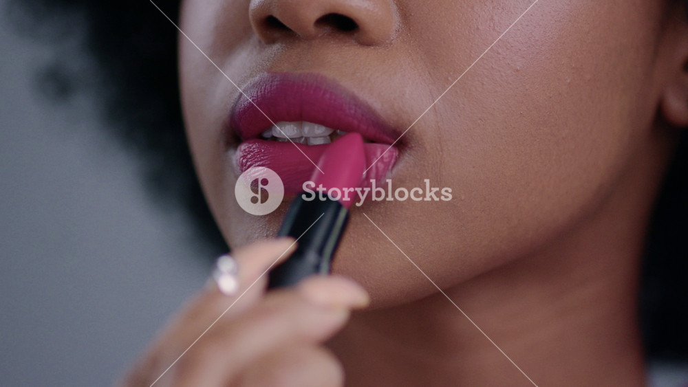 Close-up view of beautiful african girl rouging her lips with mouth opened. Lovely black woman applying pink lipstick on her lips and giving