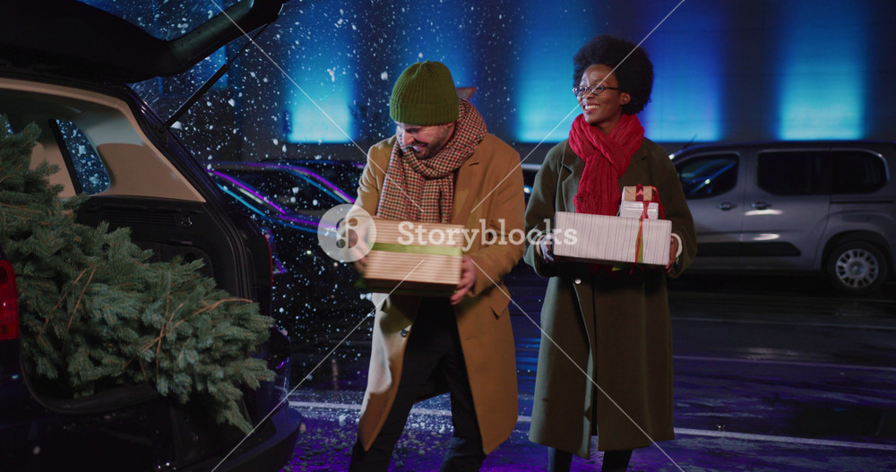 Happy beautiful multi-race young couple walking out shopping mall packing their purchases and presents in the car back. Family tradition