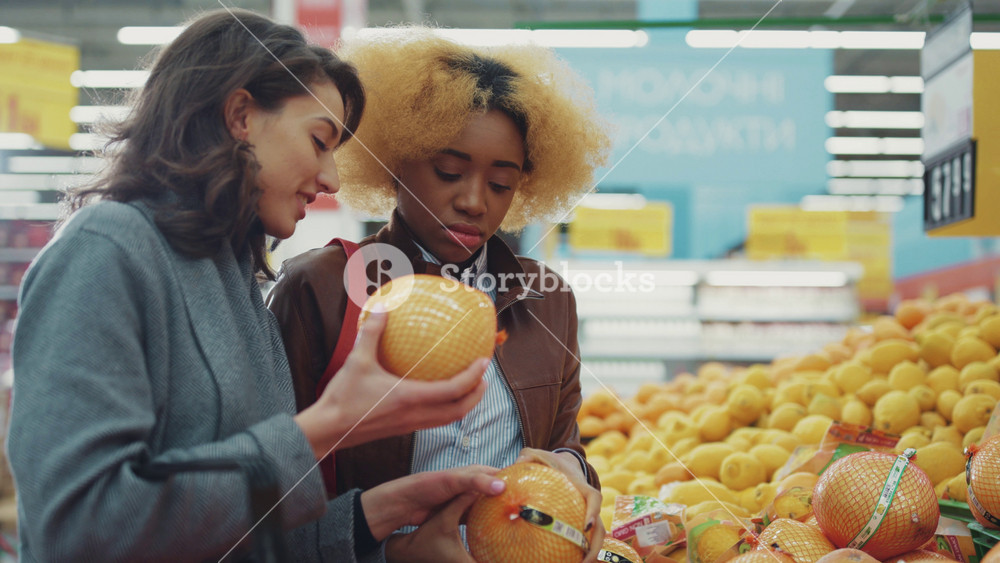 Two cute young women chooses in supermarket walk smile food shopping fruit black working consumer family buying fresh grocery market