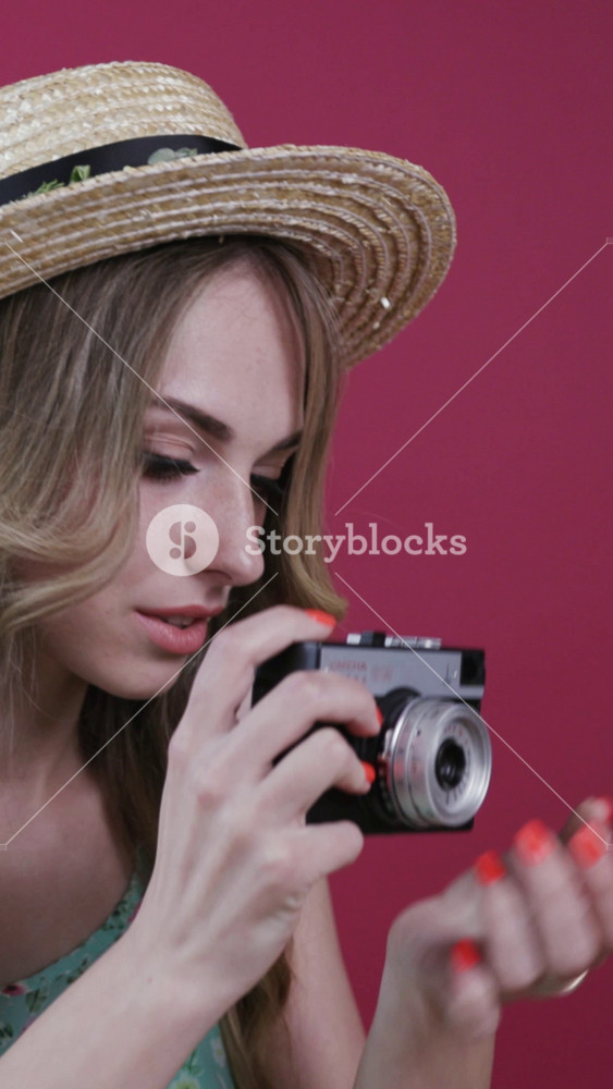 Pretty blonde caucasian woman in stylish outfit actively taking photos via retro camera on a colored background. Hobby, leisure, favorite