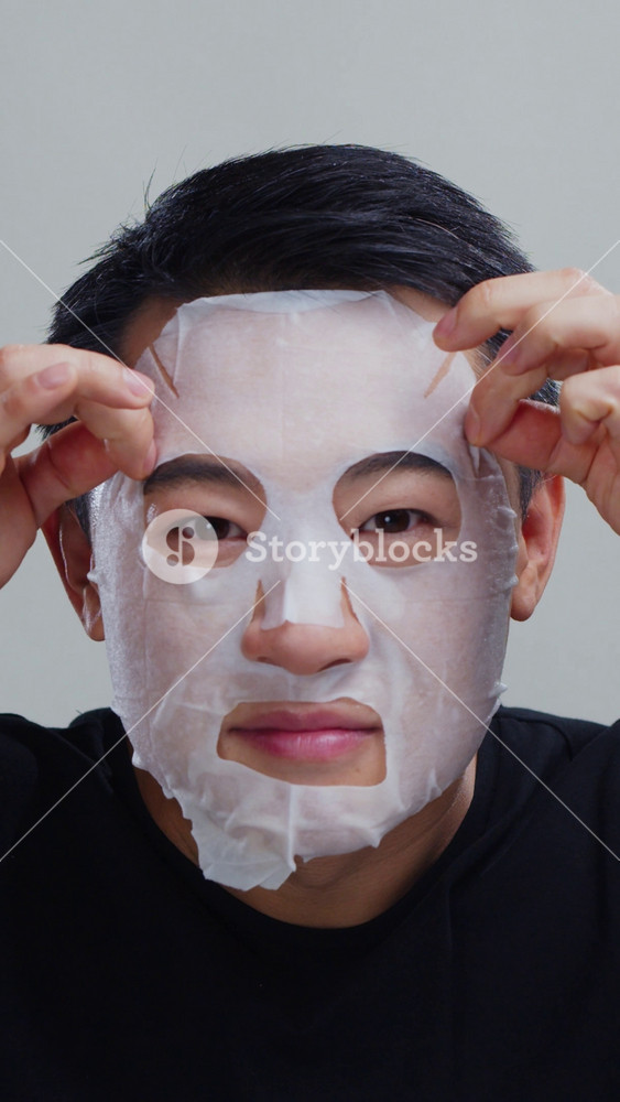 Young asian man removing sheet mask to see beautiful clear hydrated and moisturized face skin. Skincare treatment. Male model. Cosmetics.