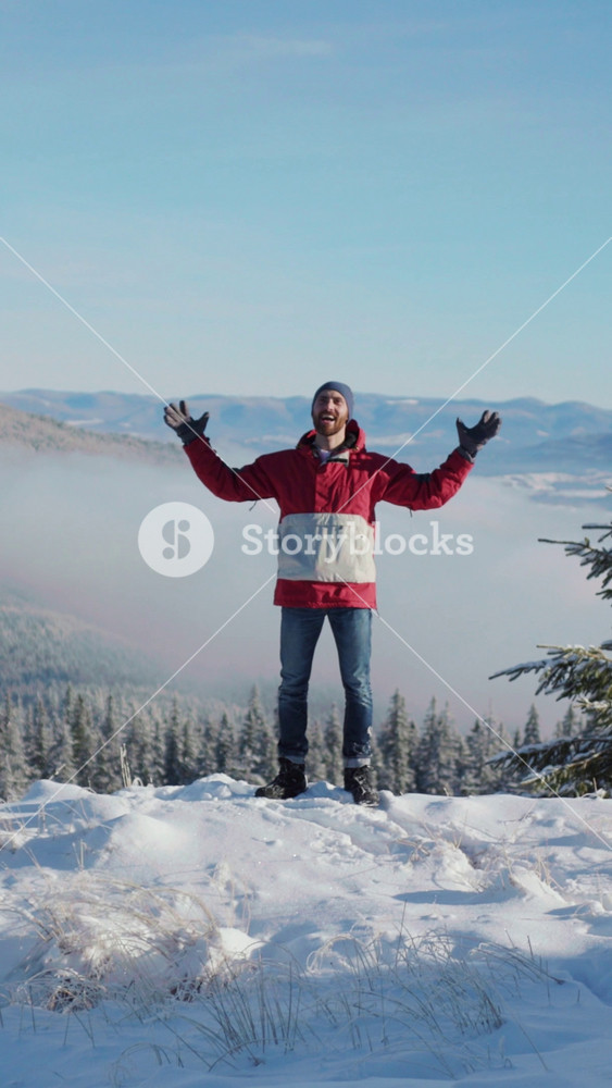 Free happy young traveler standing on mountain top spreading arms of freedom enjoying white scenery on sunny day. Travel and winter vacation