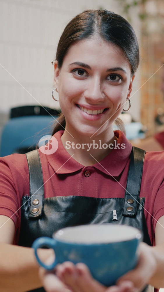Beautiful portrait of young caucasian lady barista worker servng a cup of coffee smiling positive at camera in urban cafe interior. Coffee