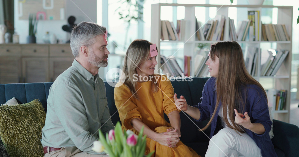 Affectionate happy family of parents and daughter playing sticker game together quessing names having fun in living room. Entertainment home