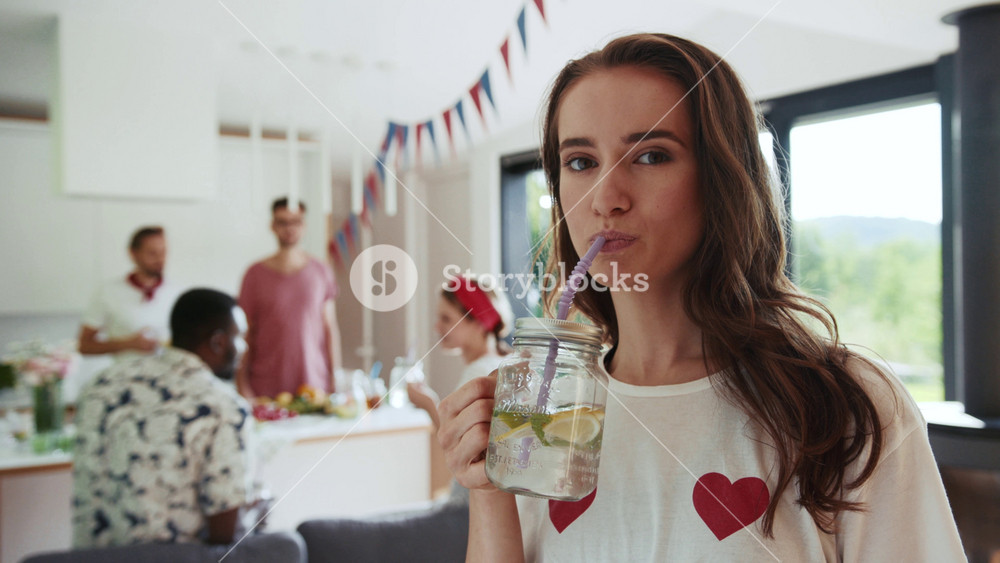 Close up view of attractive caucasian curly woman drinking fresh summer lemonade out of the mason jar with straw, and smiling seductively