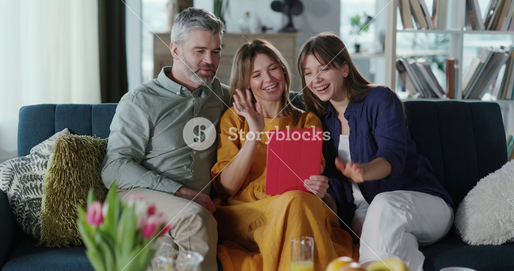 Beautiful family of adult parents and daughter celebrating mothers day and videochatting webcam tablet computer application at home. Reunion