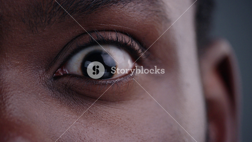 Close-up of handsome afro-american man eye wide-opebed looking straight. Detailed portrait of surprised black guy on grey background.