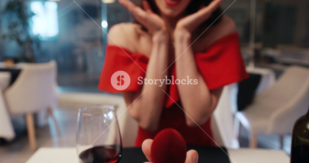 Caucasian man popping question to lovely girlfriend in popular restaurant of city. Beautiful girl in red dress accepting marriage proposal