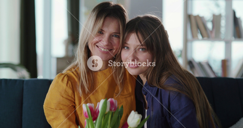 Cheerful mother and daughter embracing and holding bouquet of tulip flowers. Beautiful family couple portrait of mom and adult child smiling