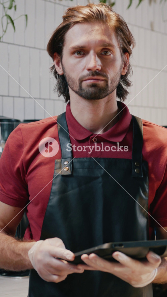 Portrait of caucasian handsome serious man worker in coffee shop. Couple of young attractive barista colleagues working at modern cafe.