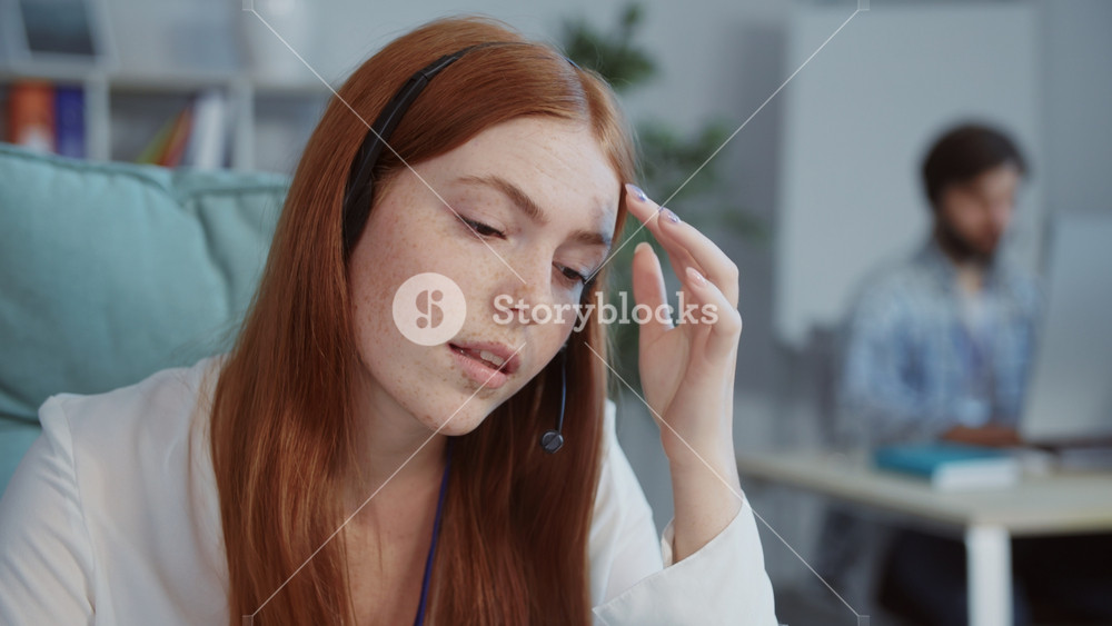 Close-up portrait of tired beautiful redhead young woman with freckles touching head. Nice girl listening to client's problem, resolving