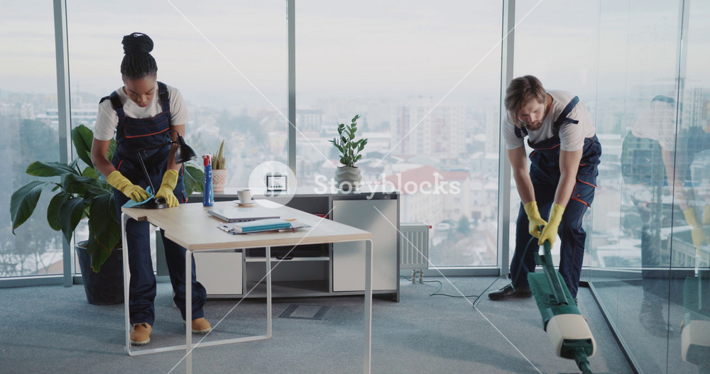 Multi-ethnic team couple of woman and man cleaning corporate office from dirt. Cleaning services people. Vacuum cleaner.