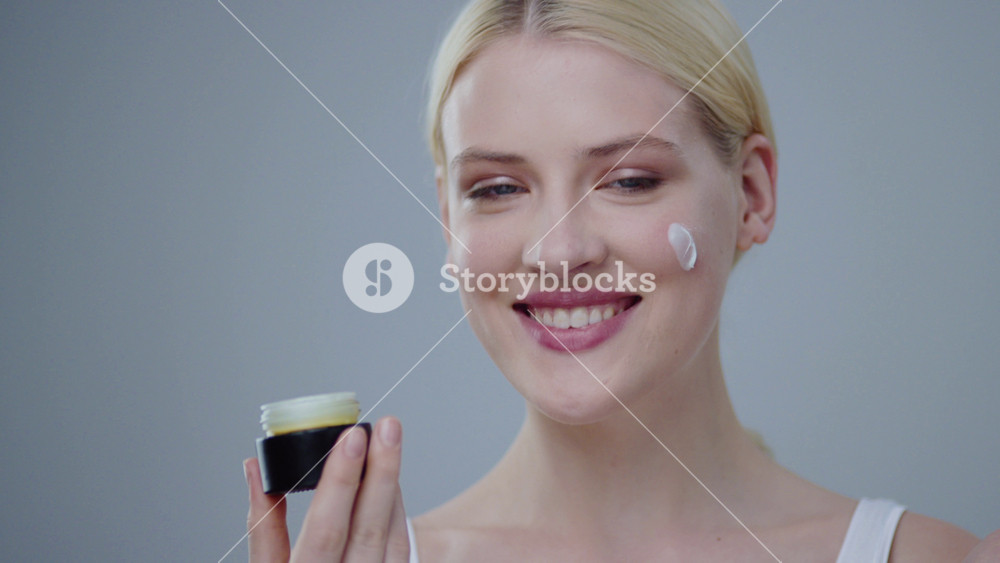 Portrait of fashion female model with natural make up in underwear on gray background. Smiling beauty young blonde woman putting cream on