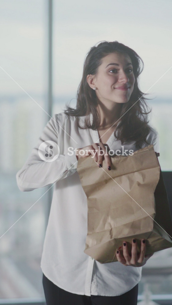 Woman checks lunch, Female employee excitedly reviews food delivery at sleek corporate workspace with courier nearby