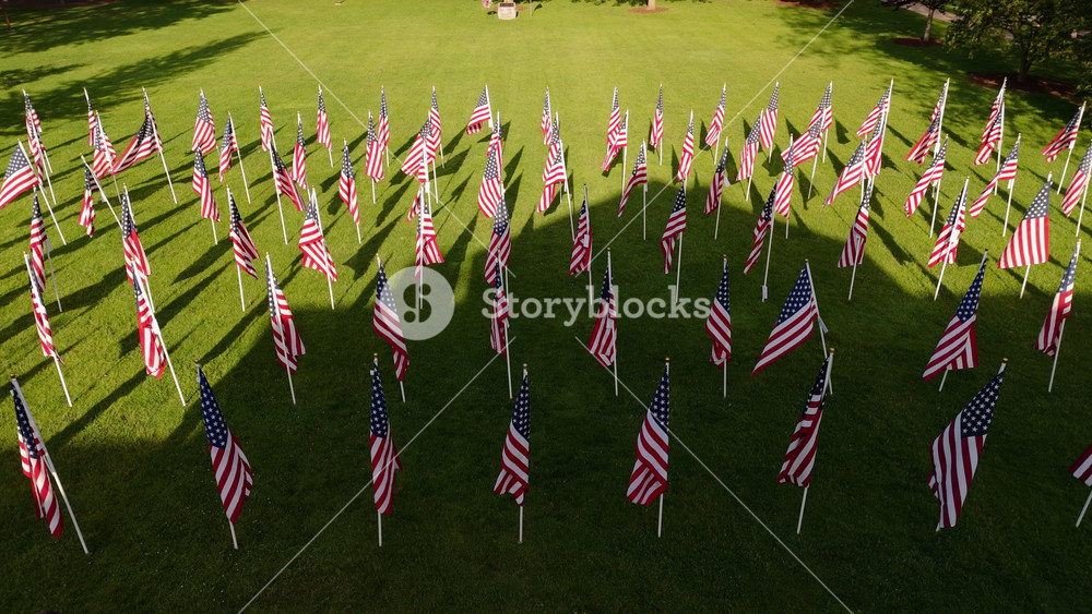 Aerial view of Many American flags blowing in the wind on green field in park on sunny day. Patriotic concept for US holidays, 4th of July