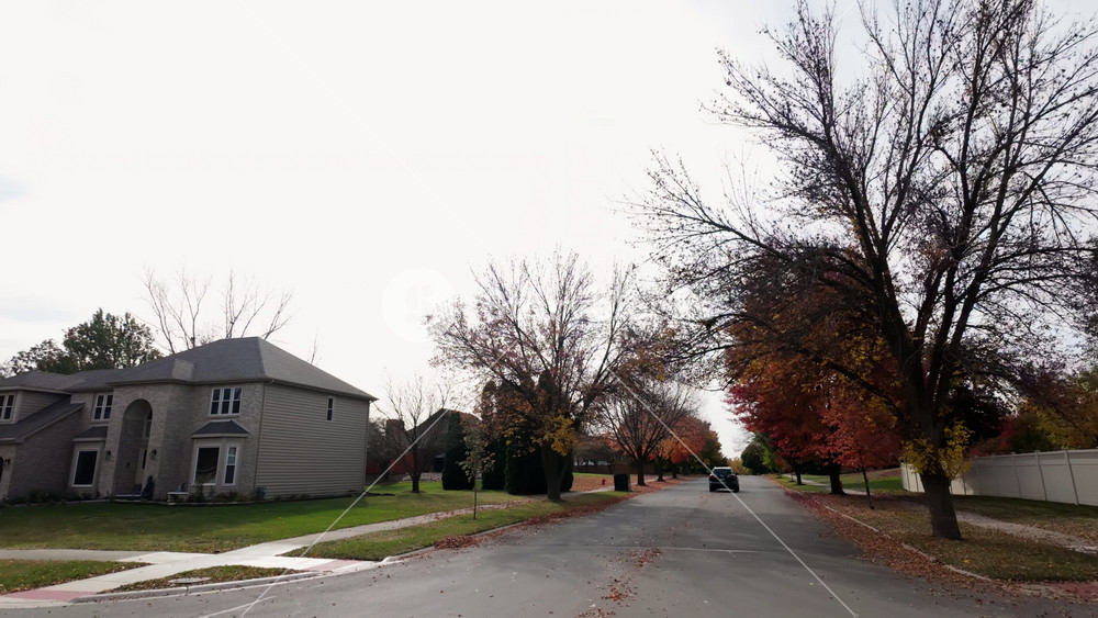 POV outside shot from the car moving along residential street with bright autumn trees. Warm colors and gloomy sky create a beautiful