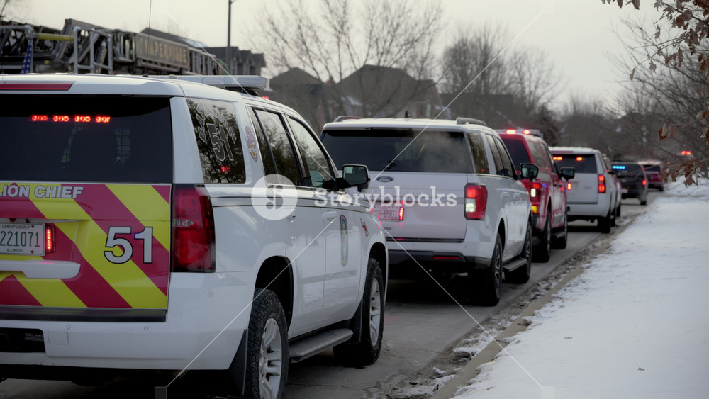 A lot of emergency vehicles with flashing lights on are parked along the city street. Rear view. Naperville IL USA. 02 February 2025