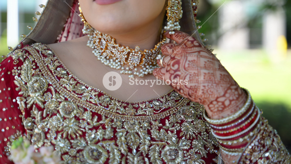 Red and gold colors in the traditional wedding Indian clothes, Close up view of embroidered dress and bride henna painted hands touching the