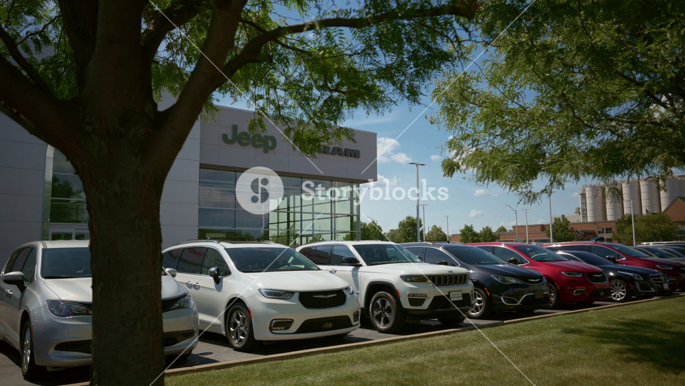 The building of Jeep, Ram dealership with many parked cars and cloudy blue sky background. logo and branding. Side view - June 27, 2025. USA