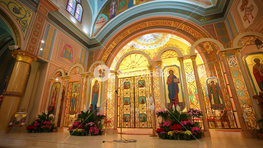 Wide view of Orthodox Christian church sanctuary featuring iconostasis, religious icons, ornate gold decorations, painted dome. Sacred