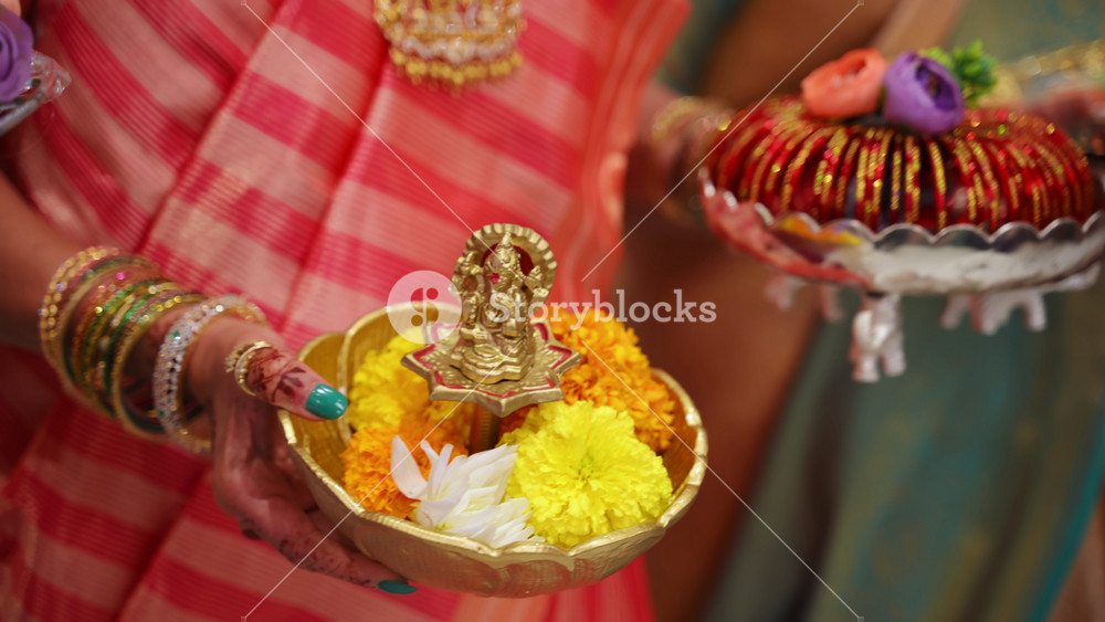 Women holding traditional offering plates with marigold flowers and ceremonial items during Indian wedding ritual. Close-up shoot of