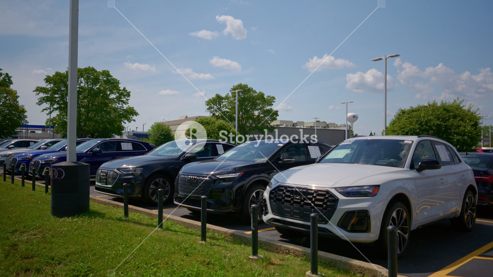 Audi dealership with a line of cars on sunny day. The dealership building displays the red Audi logo and branding. - June 27, 2025. USA, IL