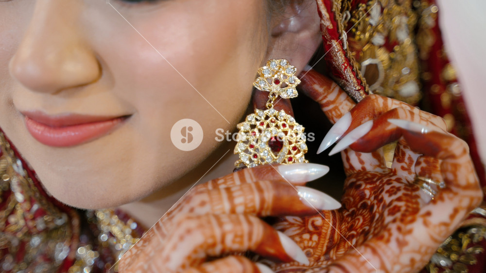 Close up of Indian bride adjusting traditional gold earring during wedding preparation. Beautiful henna details and elegant bridal jewelry.