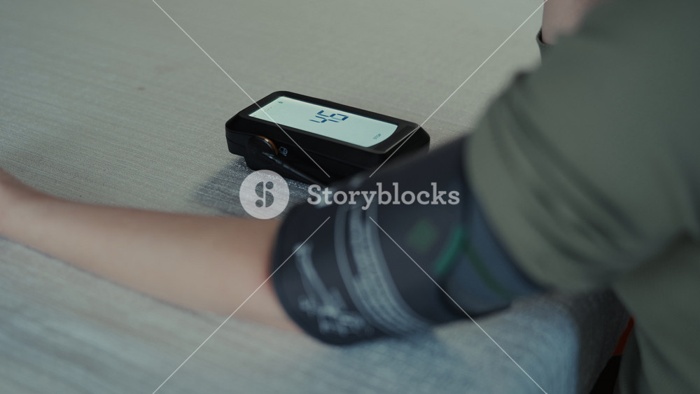 Woman sits at table and puts on blood pressure cuff to measure blood pressure using digital monitor. home healthcare, hypertension