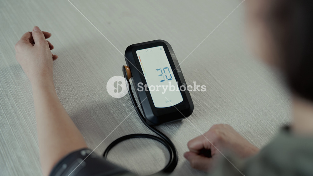 Woman sits at table and puts on blood pressure cuff and measure blood pressure using digital monitor. home healthcare, hypertension