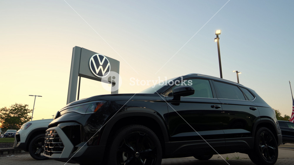 Illuminated sign post of Volkswagen car dealership and parked cars on twilight blue sky background. September 15th, 2025. USA, IL