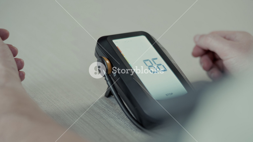 Person sit at table and puts on blood pressure cuff to measure blood pressure using digital monitor. Home healthcare, hypertension awareness