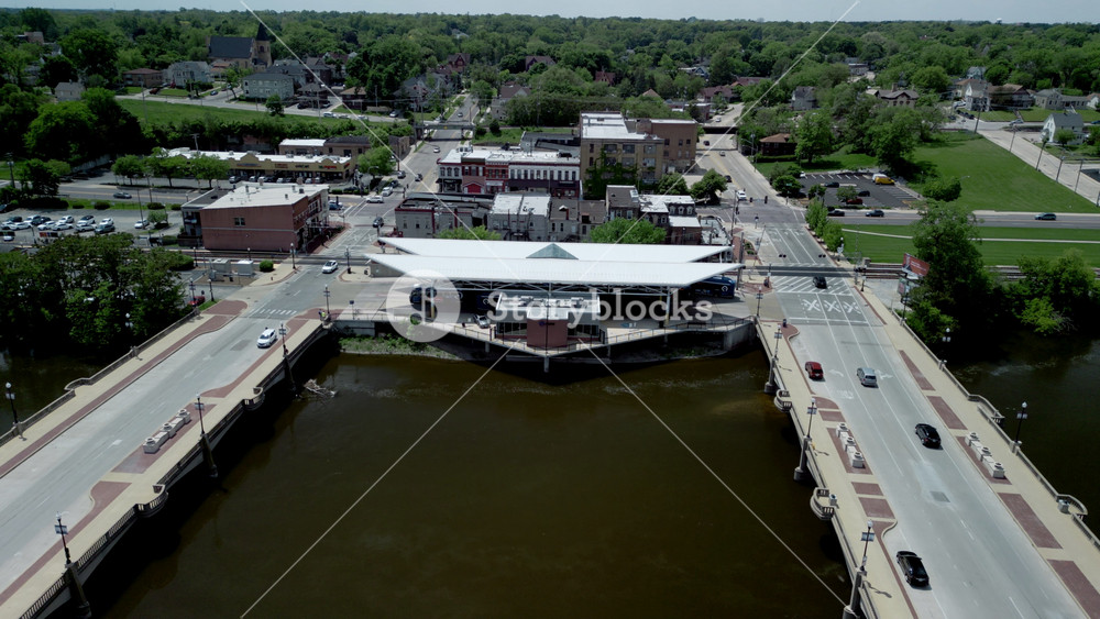 The aerial view of a Elgin town divided by Fox river, with two bridges. The town with lush greenery, a mix of residential, commercial, and