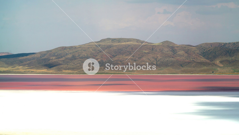 Red pink salt lake with white crust shoreline, hypersaline water and mineral deposits. Vivid magenta brine lagoon shows chalky flats, soda chemistry, halobacteria tinting.