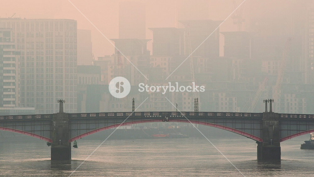 Central London City Skyline with iconic red London bus driving over Lambeth Bridge in atmospheric orange sunset with mist and fog, shot in