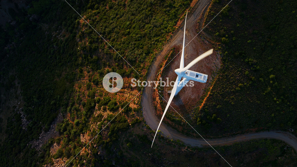 Golden sunset bathes wind farm on rolling green hills, turbines turning in aerial view to highlight clean, sustainable wind power amid scenic natural landscape