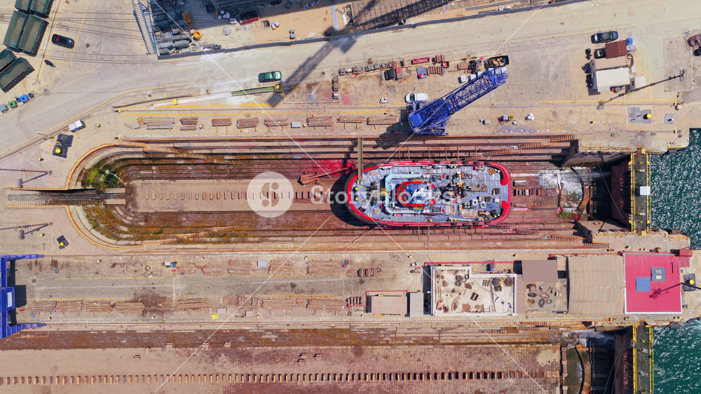 Industrial aerial view of a red tugboat launching from a shipyard's dry dock, sliding on rails into the sea for its maiden voyage after construction and maintenance in the harbor
