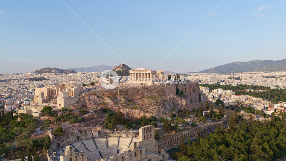 Expansive aerial view of athens, greece, showcasing the ancient acropolis citadel and the parthenon, with the sprawling cityscape and mount lycabettus visible in the background at sunset