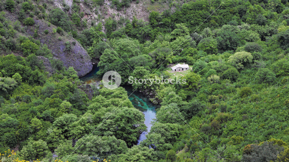 An aerial perspective of the Voidomatis River as it snakes its way through the verdant Vikos Gorge in Greece. The turquoise waters of the river contrast beautifully with the surrounding green foliage.